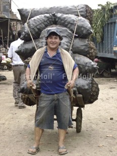 Fair Trade Photo Activity, Black, Blue, Cap, Carrying, Colour image, Dailylife, Food and alimentation, Looking at camera, Market, One man, Outdoor, People, Peru, Portrait fullbody, Potatoe, Smiling, South America, Streetlife, Strength, Vertical, Work, Working